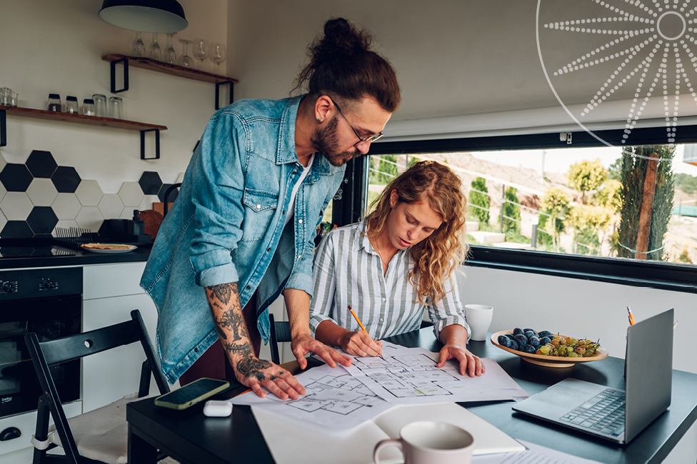 A  young man and woman reviewing floor plans over a desk in the kitchen